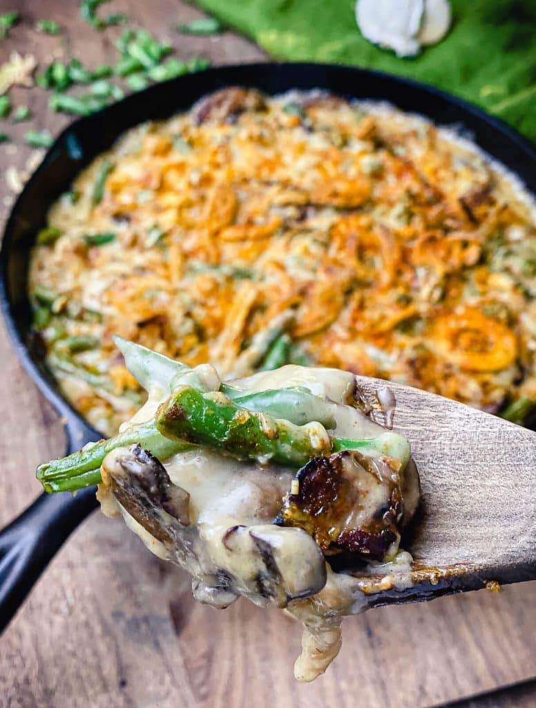 spoon of smoked green bean casserole in front of cast iron pan