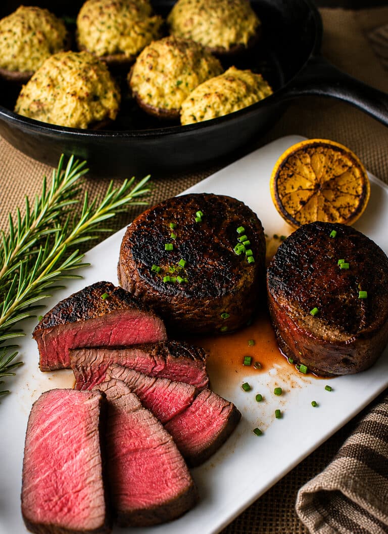 sous vide filet mignon sliced on a white plate with fresh rosemary and charred lemon