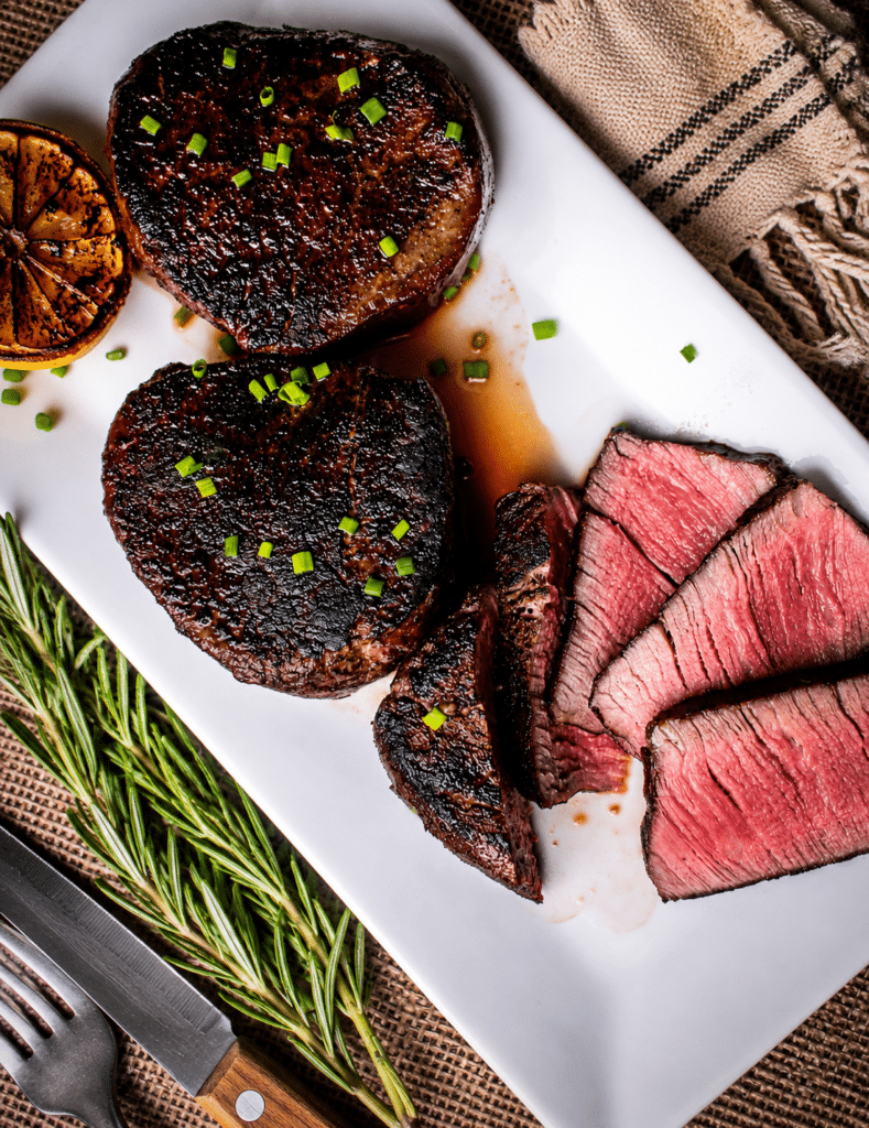 Sous vide filet mignon sliced to show an even edge to edge medium rare interior, plated with charred lemon and rosemary