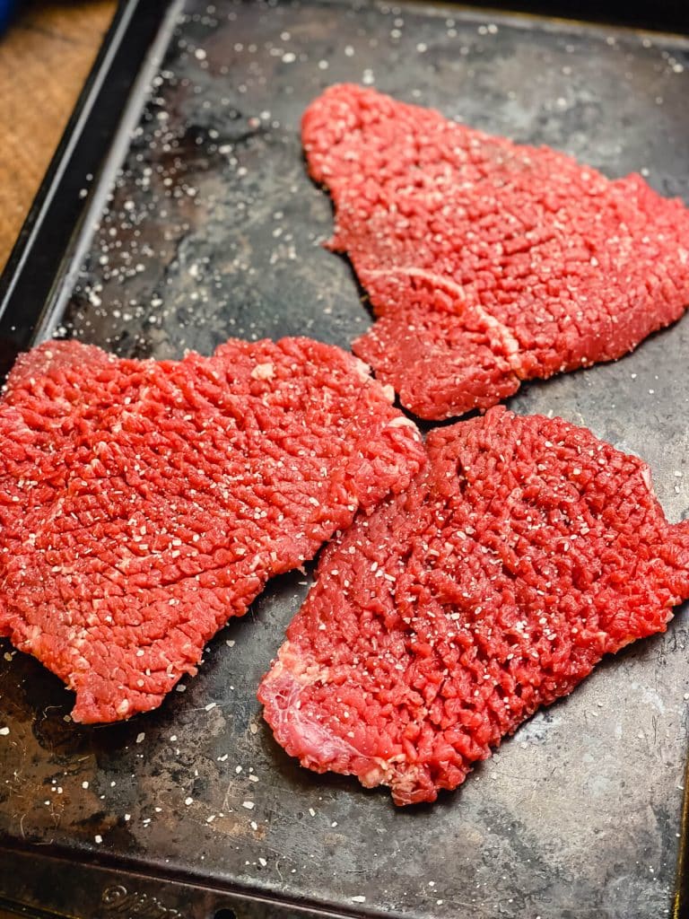 seasoned cube steaks on a baking sheet