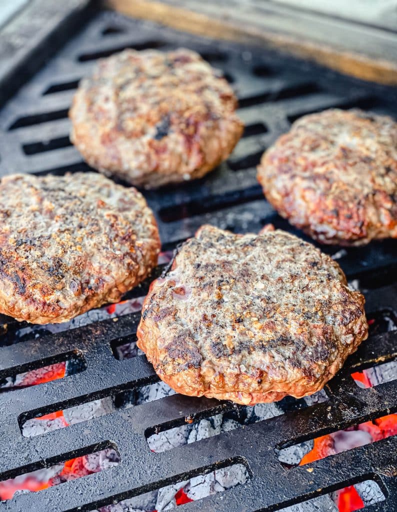 venison burger patties on the grill over charcoal