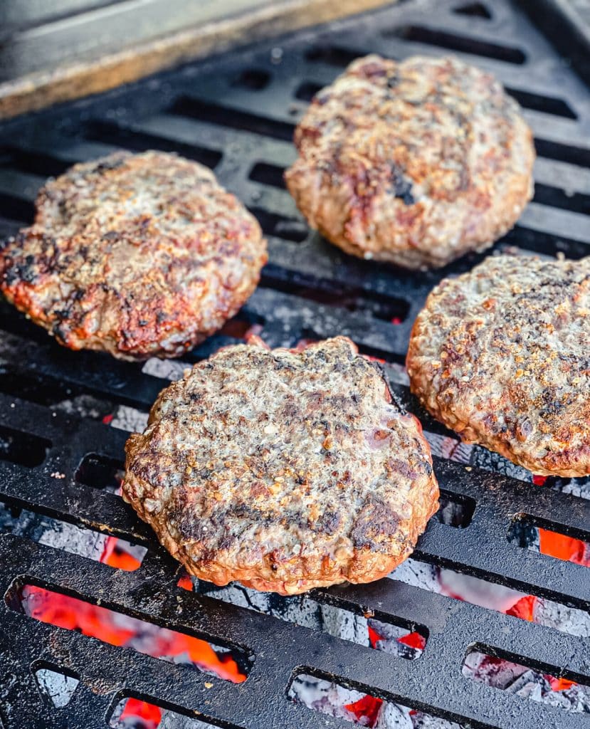 venison burgers being cooked over charcoal on the grill