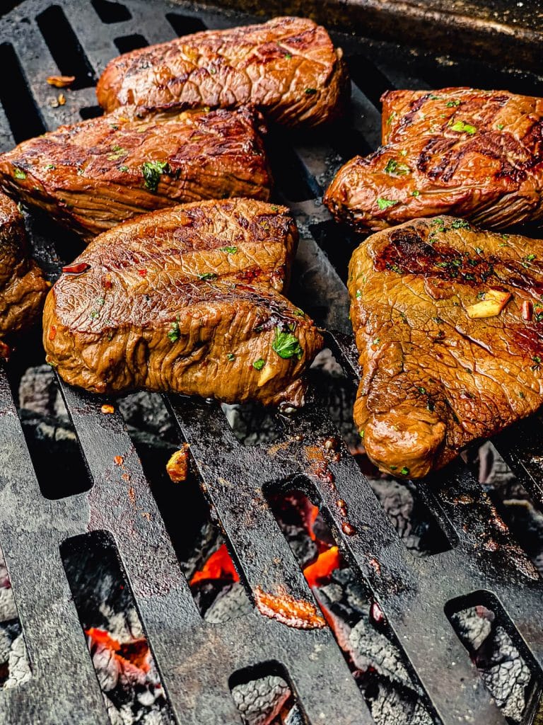 venison steaks grilling over charcoal