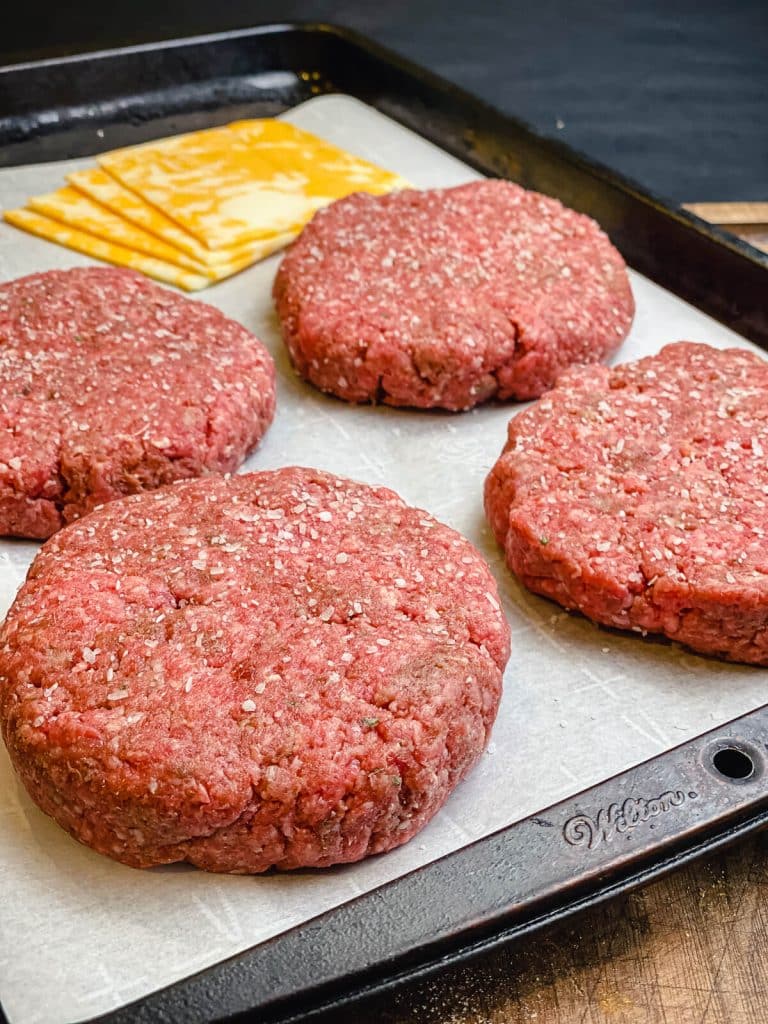 burger patties on a sheet tray with cheese