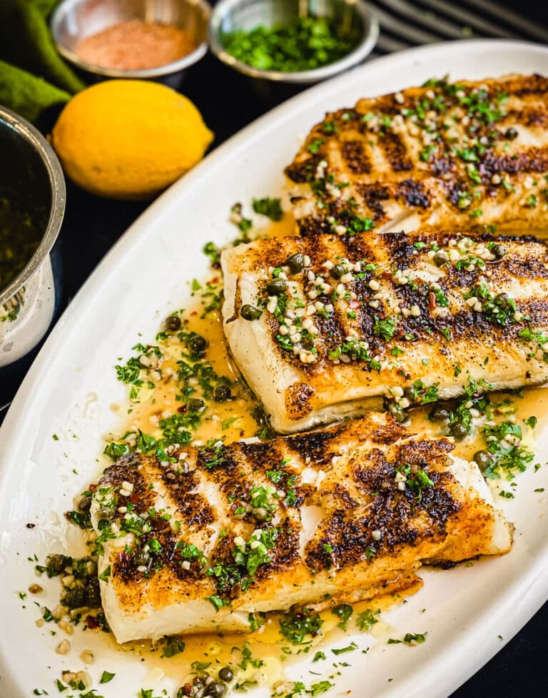 grilled chilean sea bass on a platter with lemons and sauce