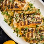 grilled chilean sea bass on a platter with lemons and sauce drizzle