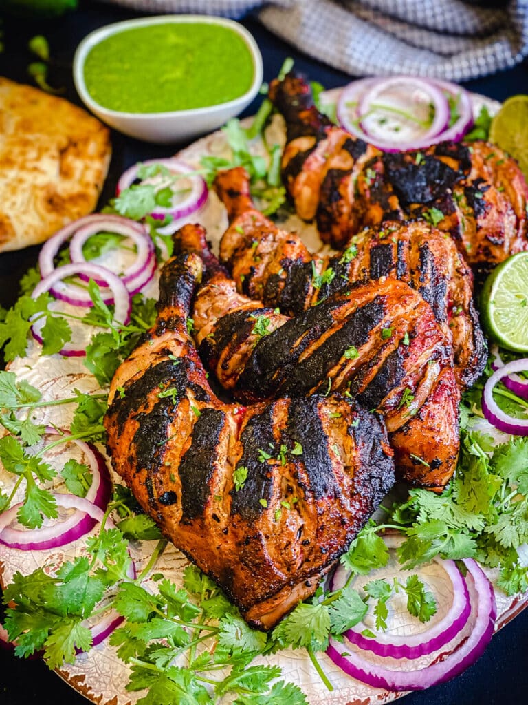 grilled tandoori chicken on a platter with cilantro and onions