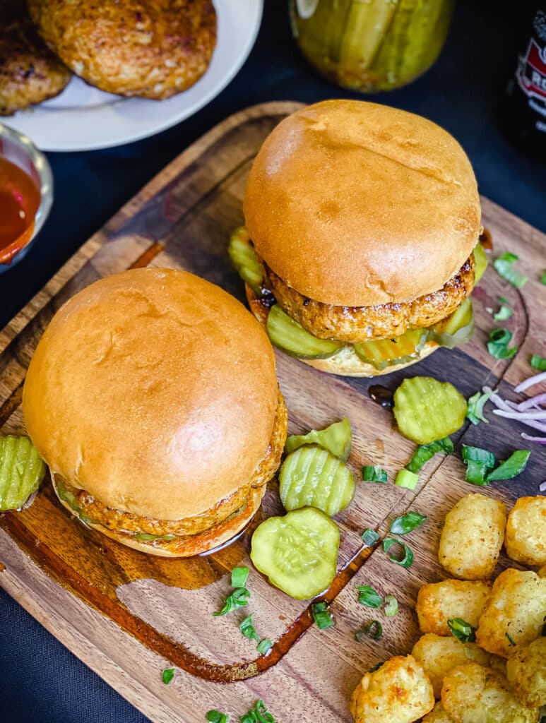 Nashville hot chicken burgers on a wood plate with hot sauce