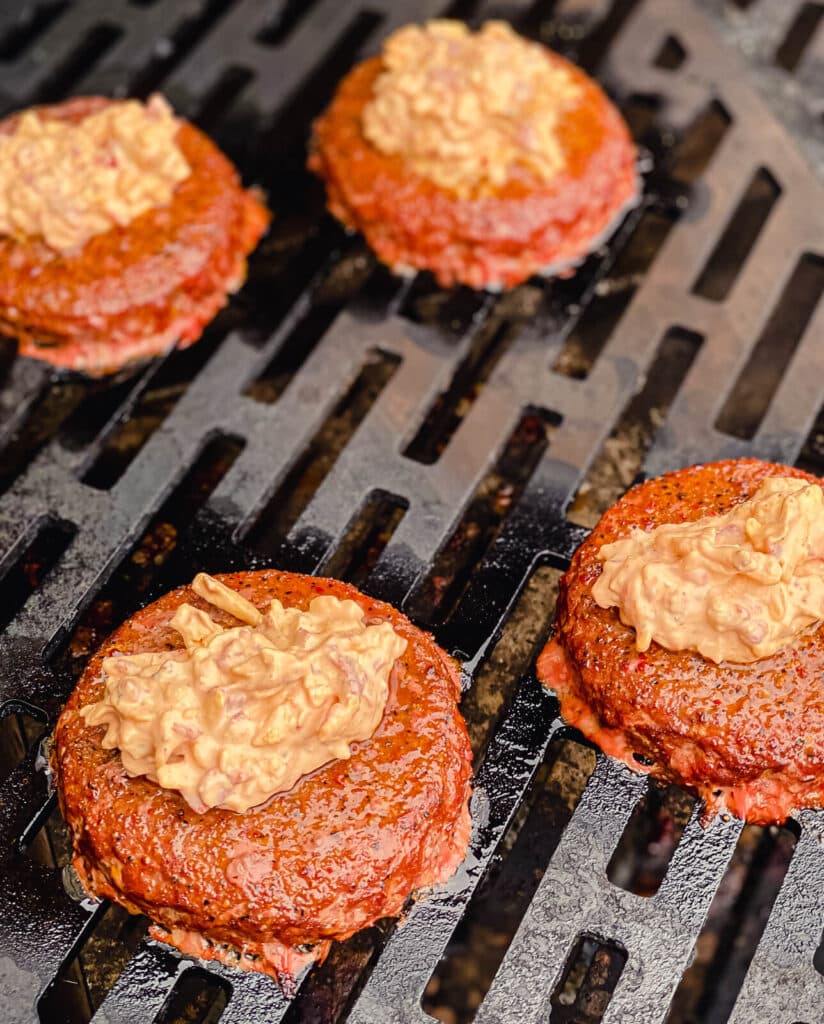 pimento cheese on top of burger patties on a grill