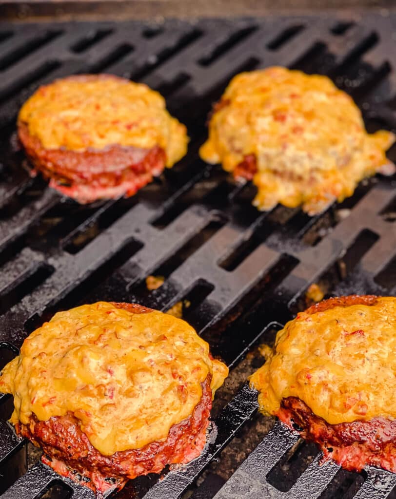 melted pimento cheese on burger patties on a grill