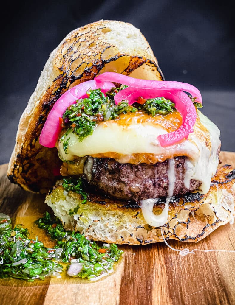 provoleta burger on a cutting board with pickled red onions