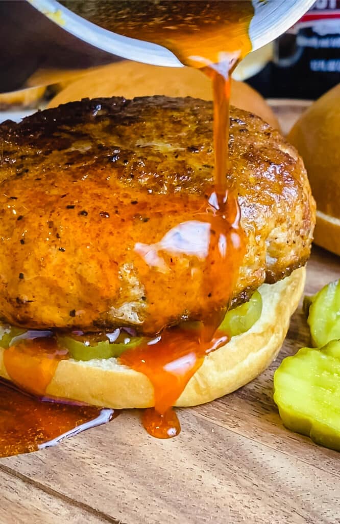 sauce being drizzled on a Nashville hot chicken burger