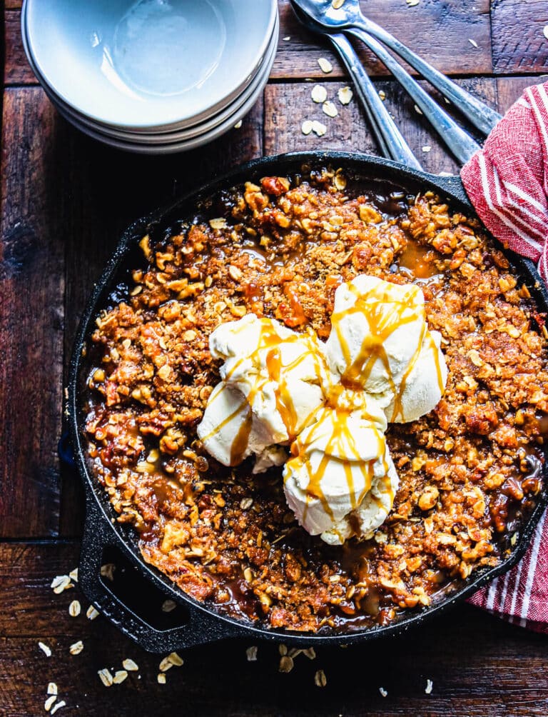 smoked apple crisp in a cast iron pan on a wood table with bowls and spoons