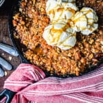 smoked apple crisp in a cast iron pan with red towel wrapped around the handle