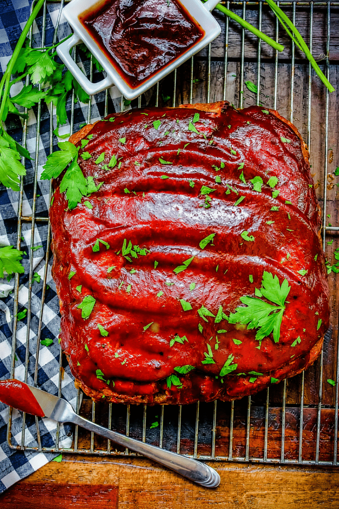 smoked meatloaf sitting on a cooling rack and dressed with bbq sauce