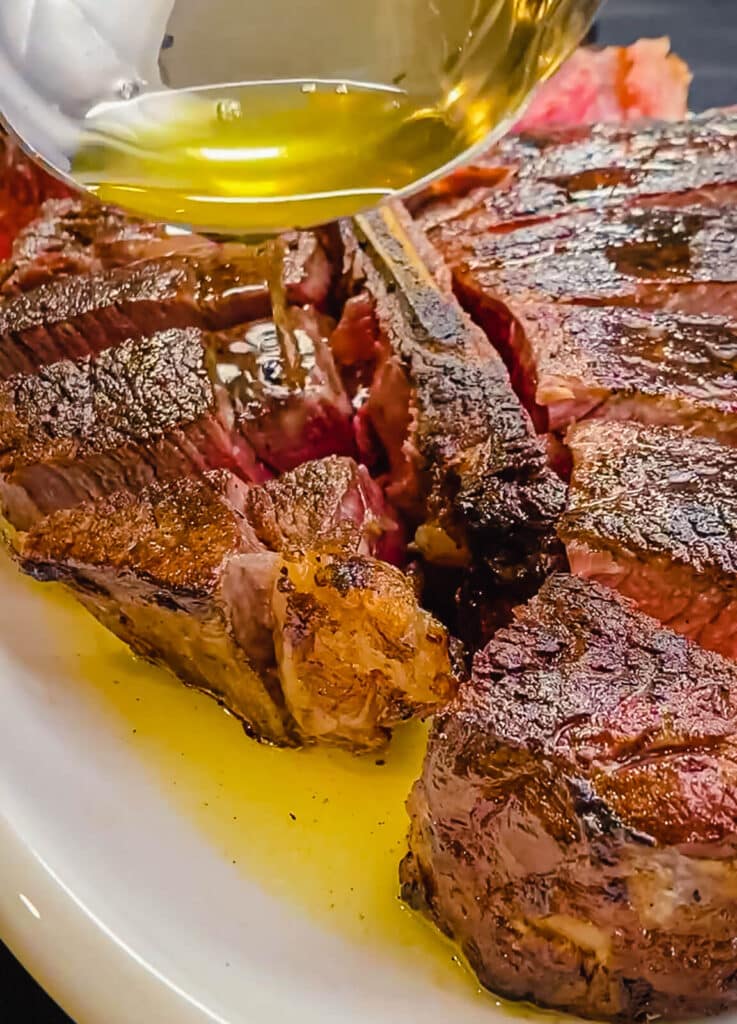 Clarified butter being drizzled onto a porterhouse steak on a platter