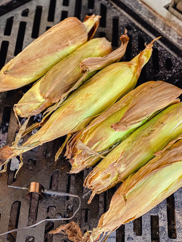 corn on the cob in the husk roasting on a grill