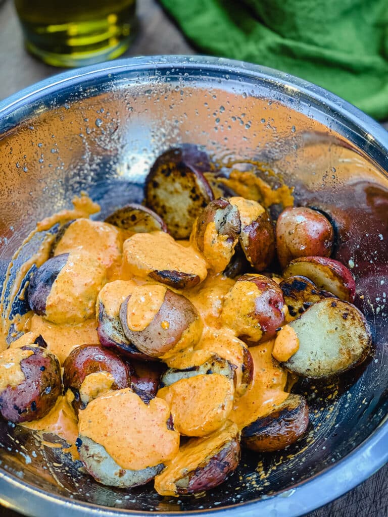 grilled potatoes in a mixing bowl with potato salad dressing