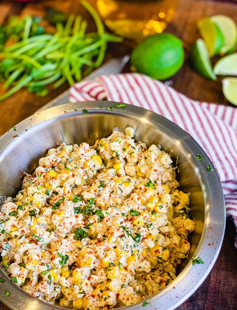 esquites mixed in a large bowl sitting on a cutting board with limes and a knife