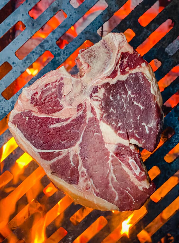porterhouse steak on a grill grate over flames