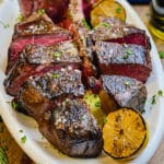 steak florentine sliced on a platter with grilled lemons