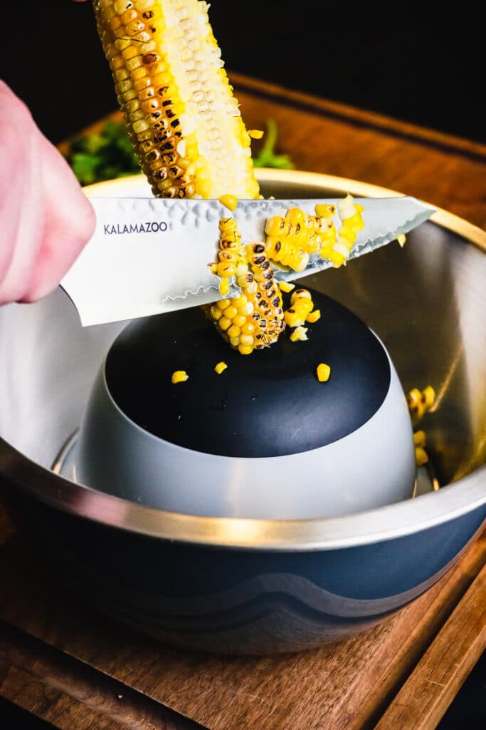 corn being sliced off the cob into a bowl