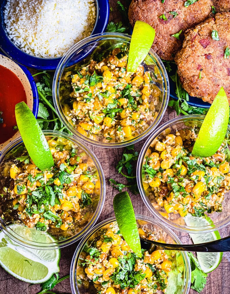 cups of esquites Mexican corn salad with limes sitting on a cutting board