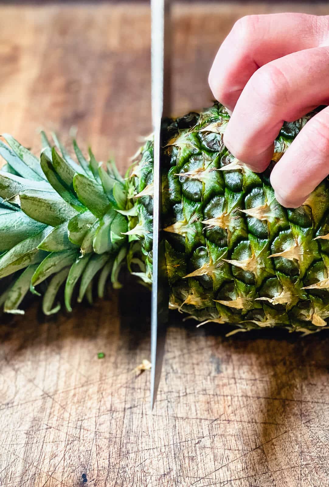 knife cutting off the top of a pineapple