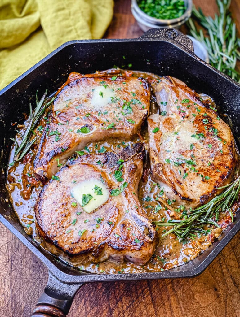 pan seared pork chops in a cast iron pan, with rosemary and butter