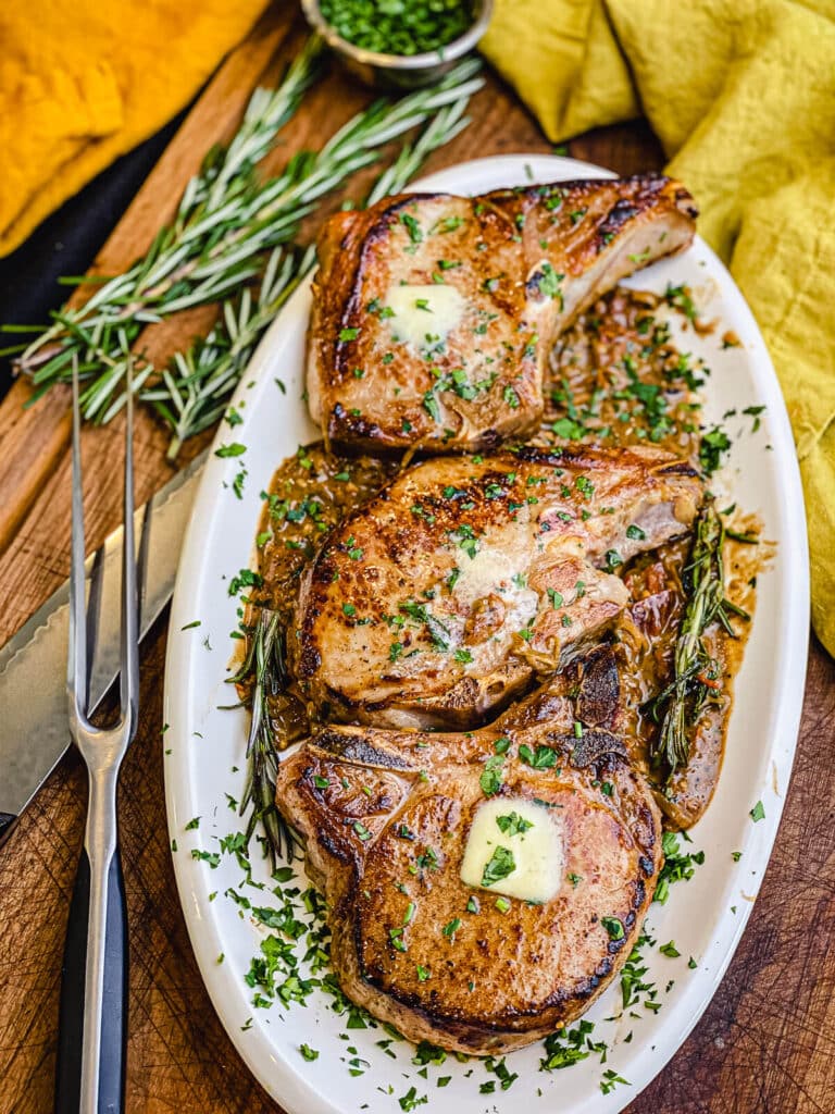 pan seared pork chops on a platter with rosemary and a knife in the background