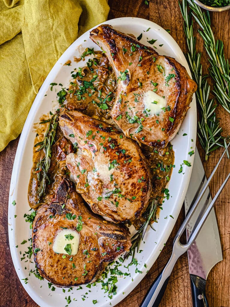 platter of pan seared pork chops with a knife and cutting prong 