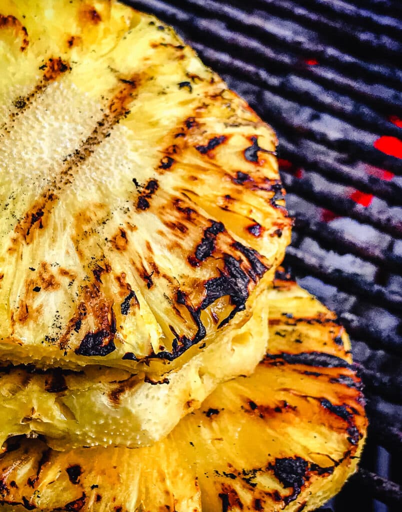 charred pineapple slices on a grill grate over flame