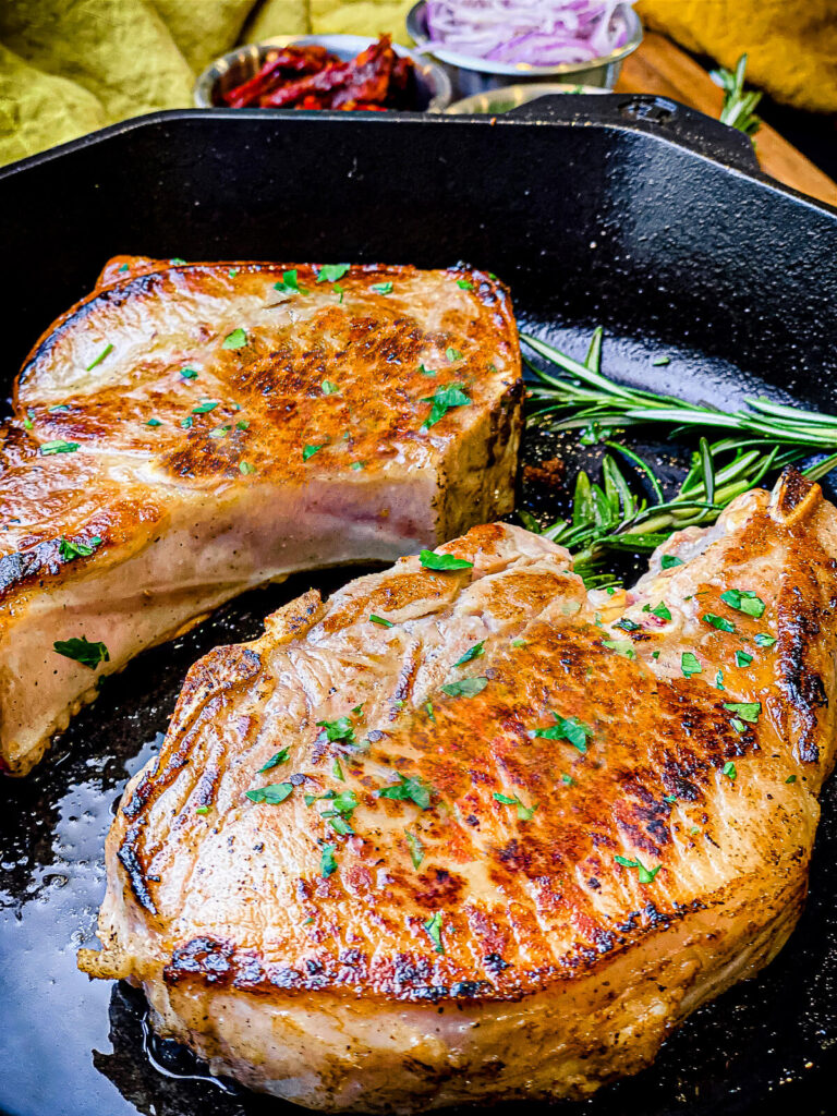two bone-in pork chops searing in a cast iron pan