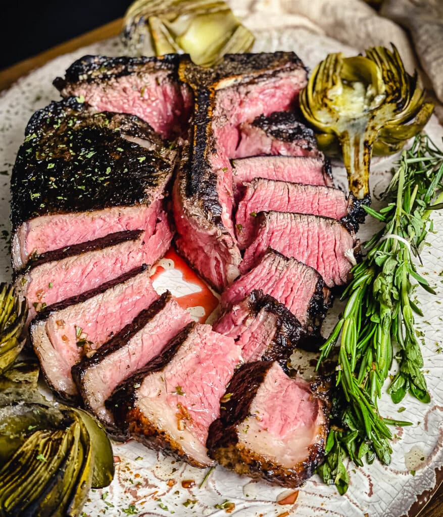 tuscan style porterhouse steak with artichokes and herbs on a platter