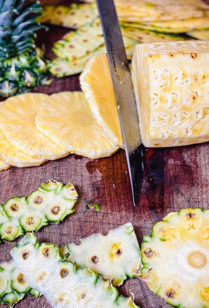 a knife blade slicing a pineapple into thin slices on a cutting board