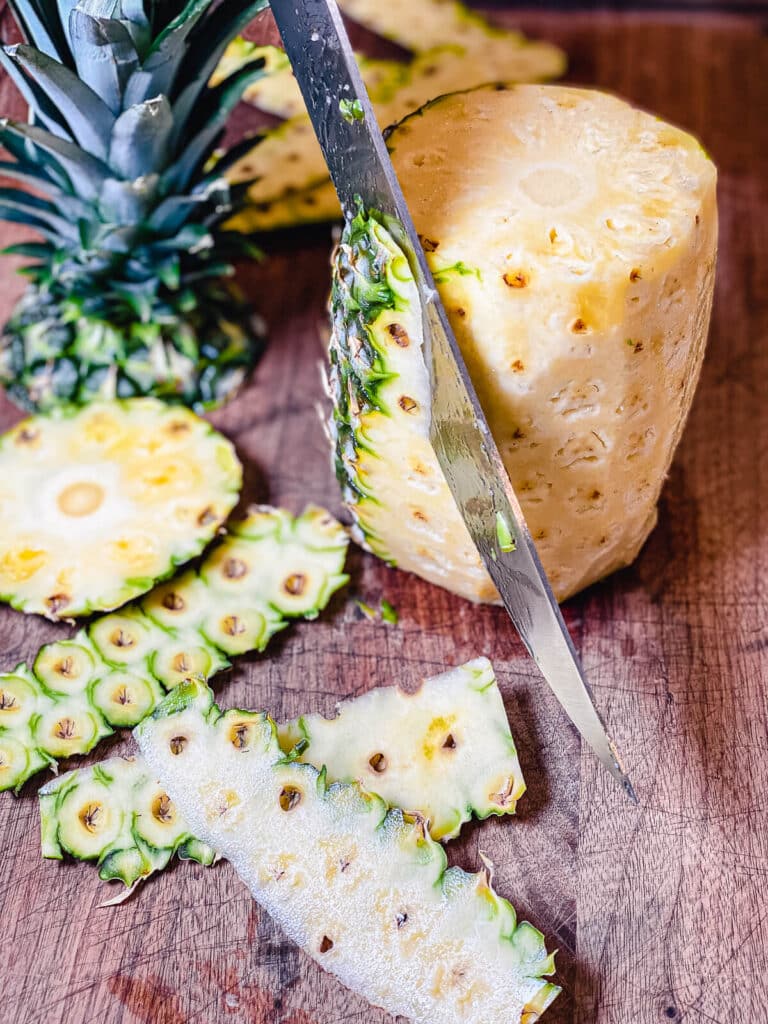 knife blade slicing the skin off of a fresh pineapple