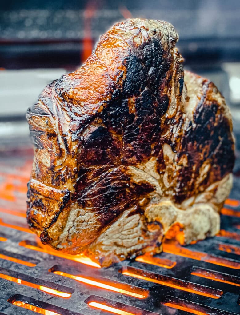 steak florentine being grilled on its edge over flames on a grill