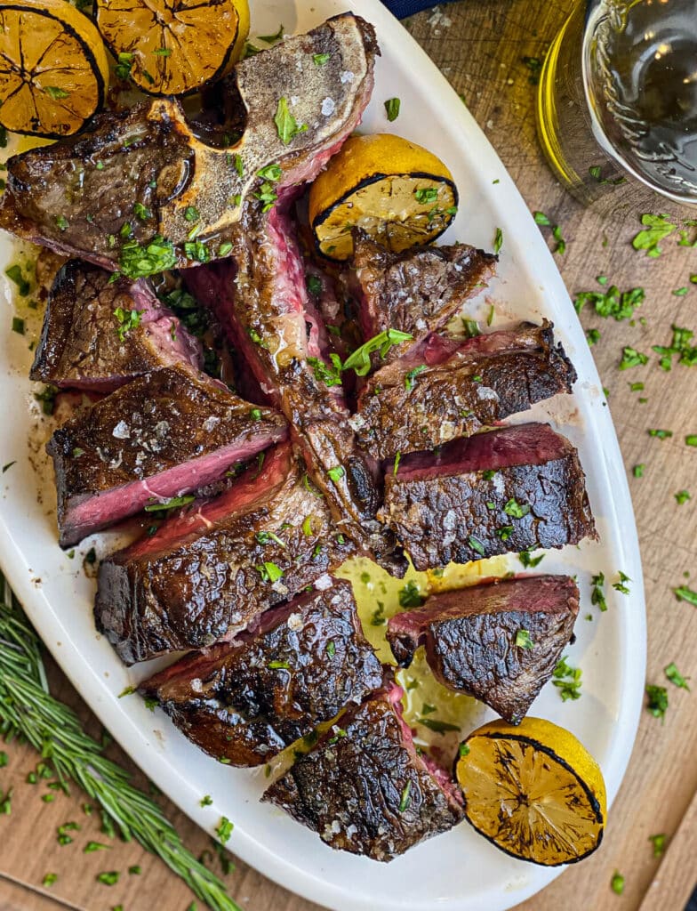 overhead shot of steak florentine sliced on a white platter with grilled lemons