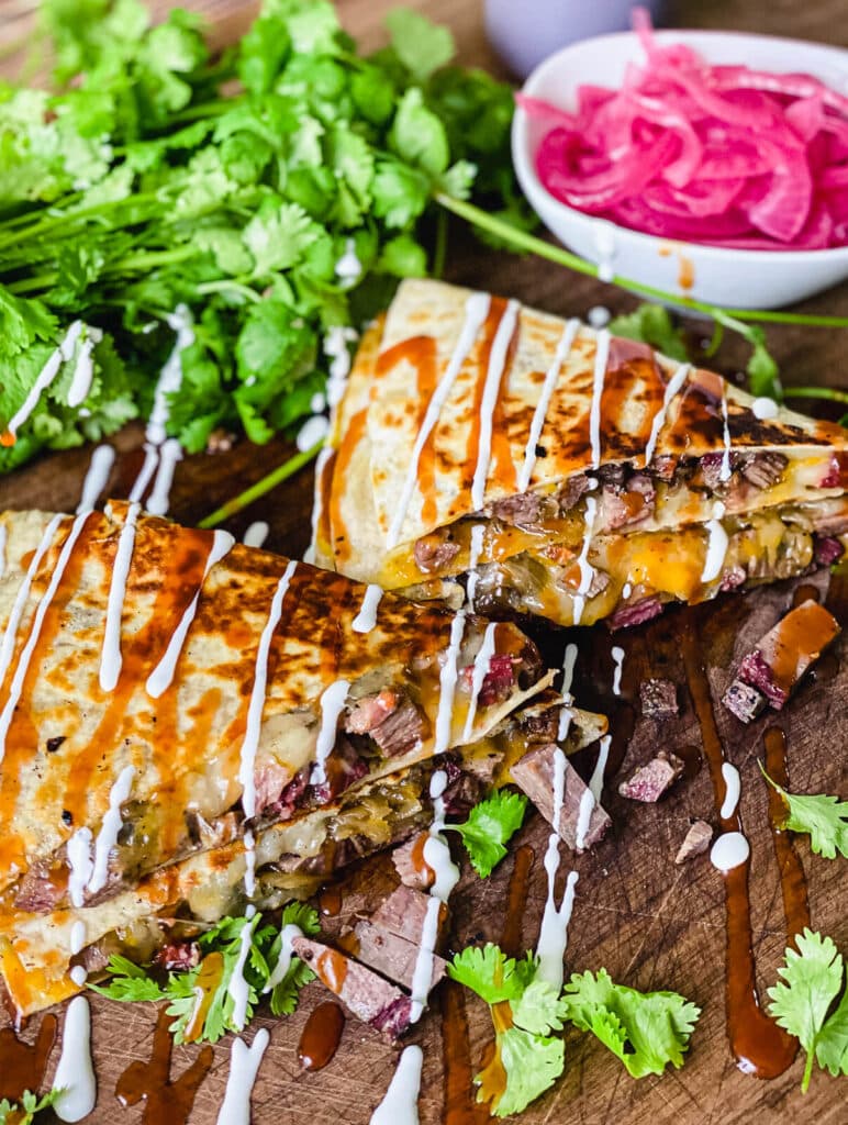 steak quesadilla on a cutting board drizzled with sour cream and bbq sauce