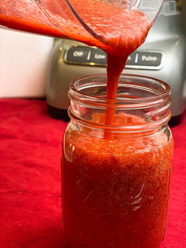 strawberry puree being poured into a mason jar