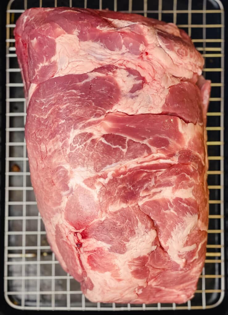 uncooked pork shoulder sitting on a wire rack