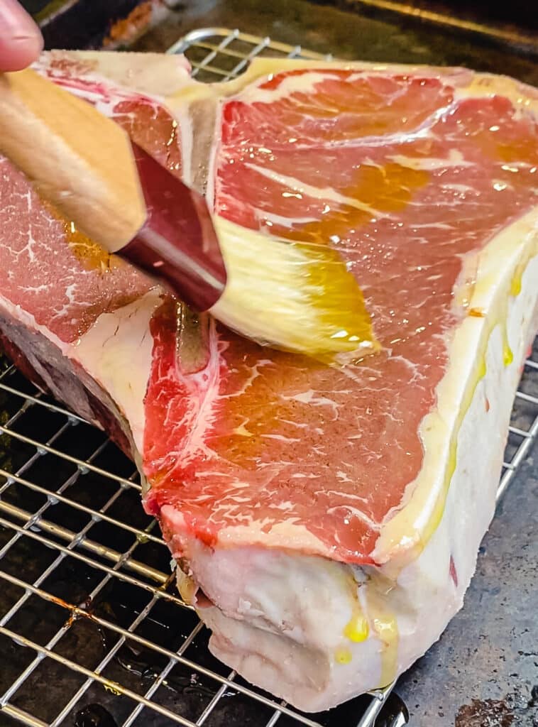 olive oil being brushed onto a raw porterhouse steak