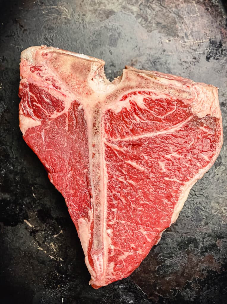 uncooked porterhouse steak on a black tray