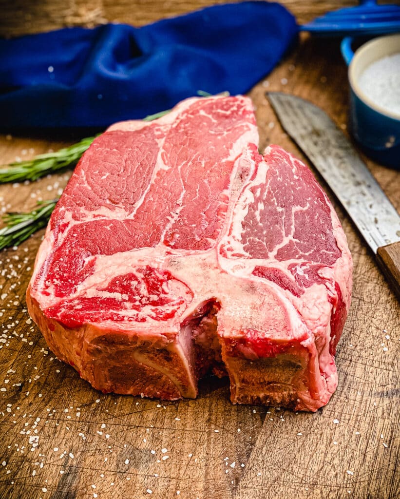 raw porterhouse steak sitting on a cutting board with a knife