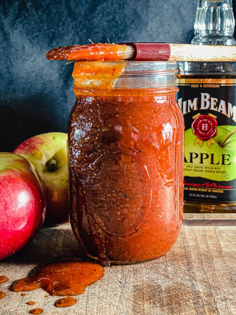 a jar of apple whiskey bbq sauce with a bottle of whiskey in the background