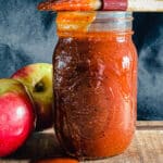 Jar of apple whiskey BBQ sauce with a brush on top and apples in the background