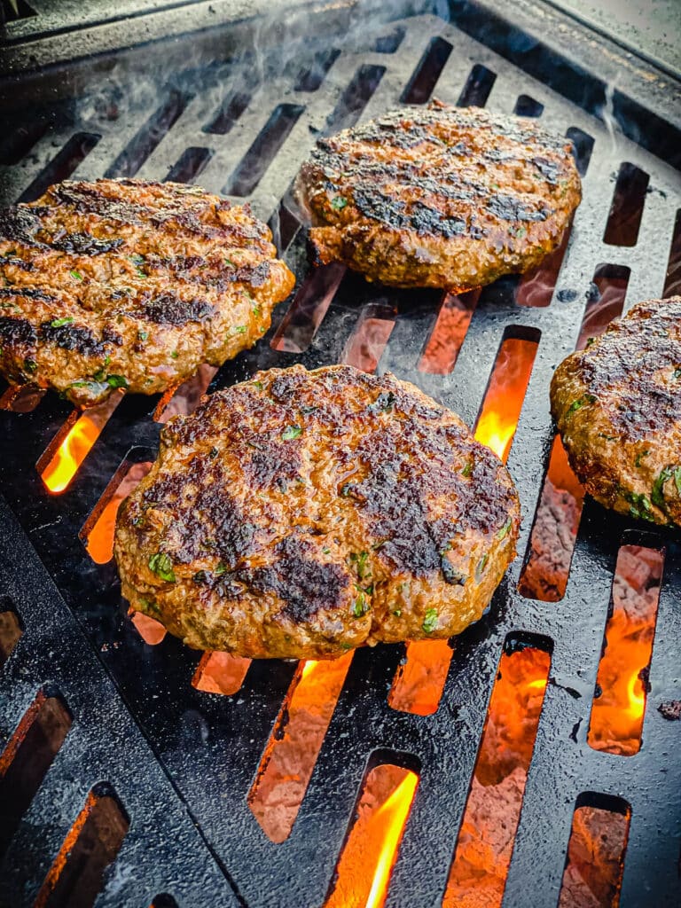 charred burger patties on a grill grate over hot coals