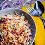 a bowl of no mayo coleslaw in a bowl with a fork and a spoon next to it