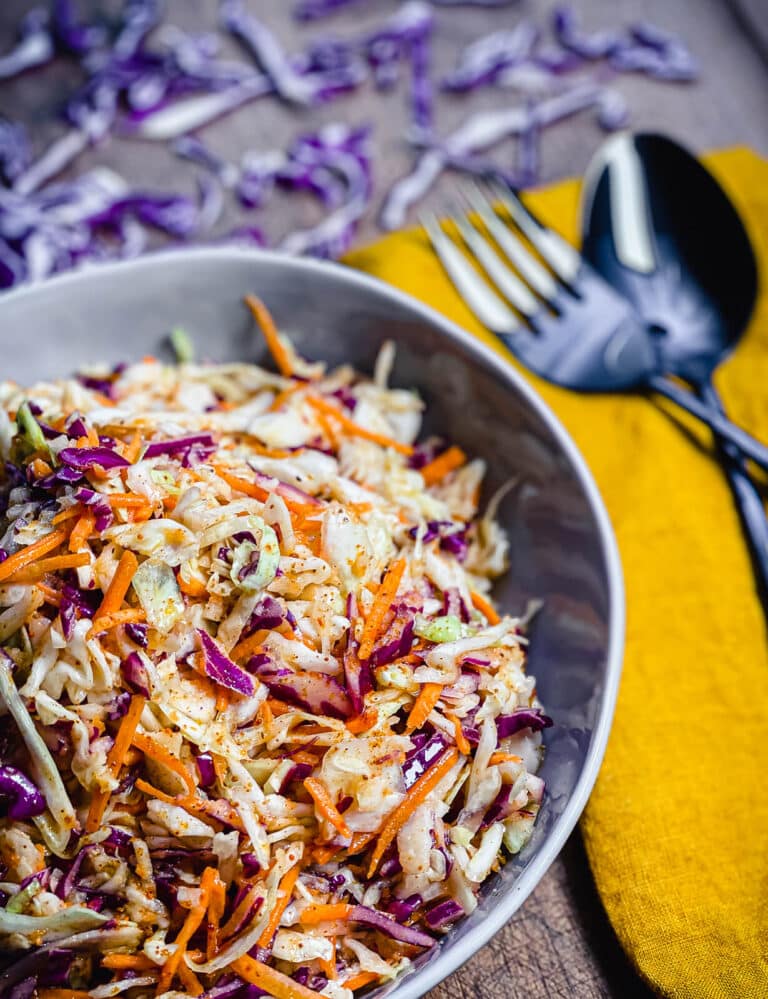 a bowl of no mayo coleslaw in a bowl with a fork and a spoon next to it