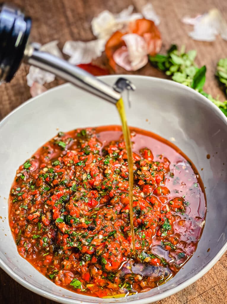 olive oil being added to a bowl of red chimichurri